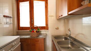 A kitchen with wooden cabinets, a granite countertop, a stainless steel sink, and a window with a lace curtain.