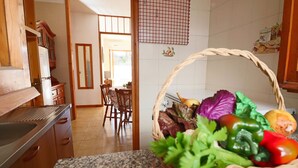 A kitchen with granite countertops, wooden cabinets, a dining area with chairs, and a basket of fresh vegetables on the counter. - Nice House Cecilia in Otranto (Otranto)