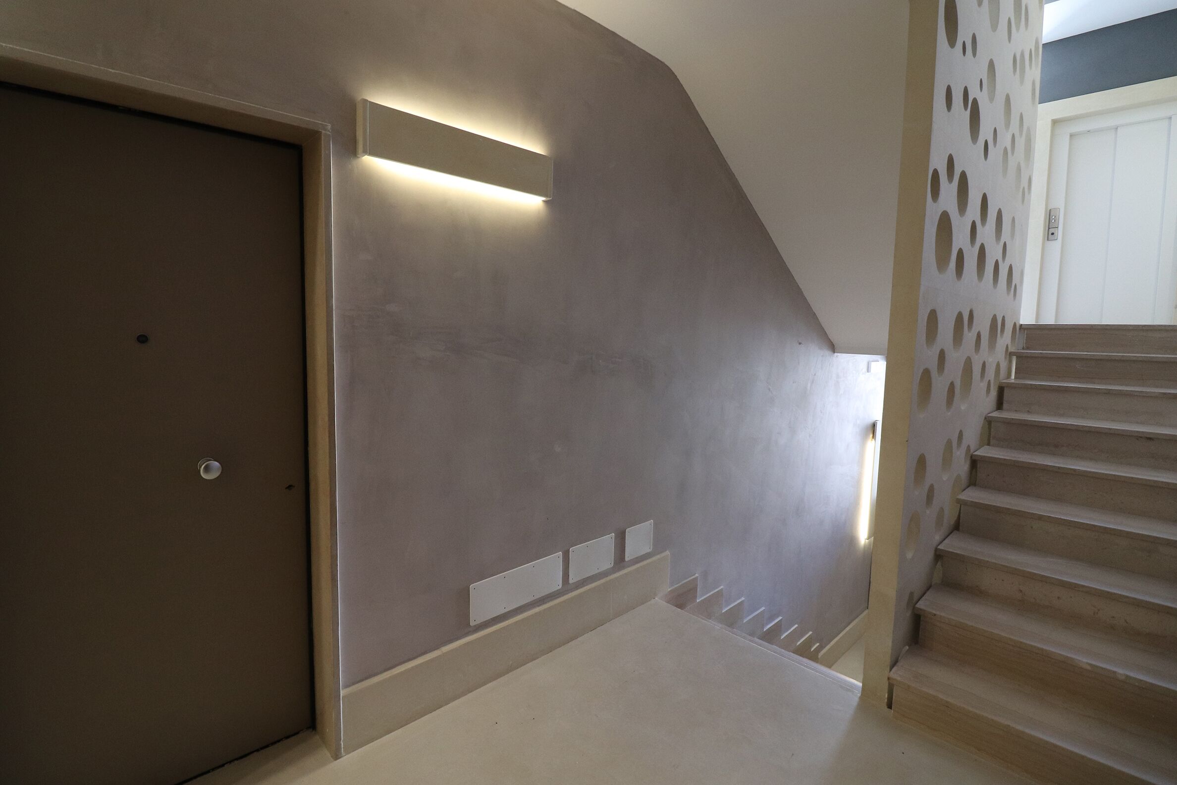 Ein modernes Interieur mit Treppe, Tür und Wand mit eingelassener Beleuchtung.