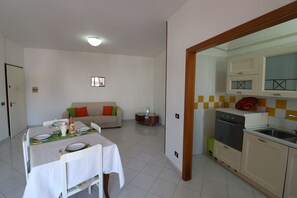 A dining area with a table set for four, a sofa, a small side table, and a kitchen with a sink and stove.