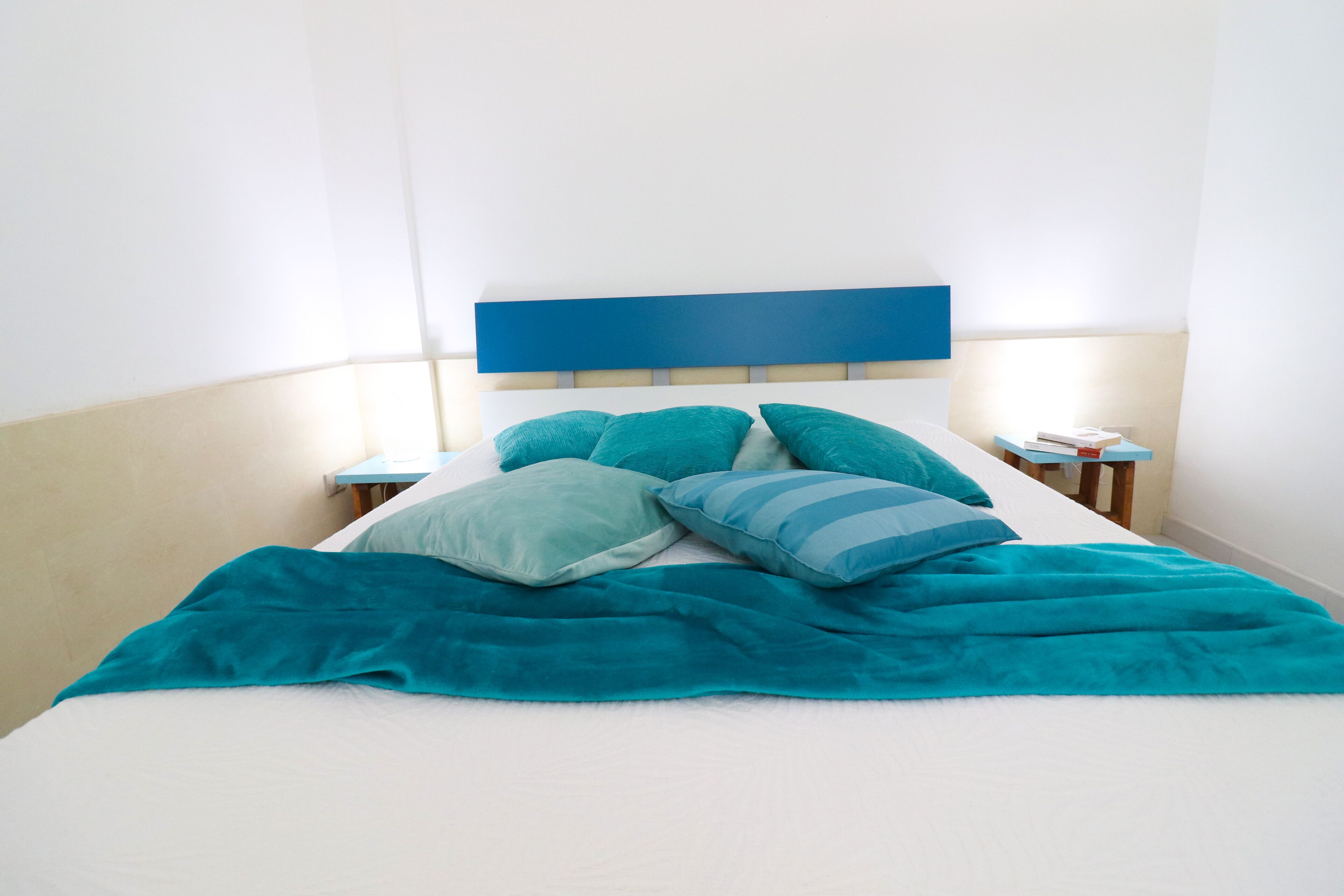 A bed with a blue headboard, teal pillows, and a teal blanket.