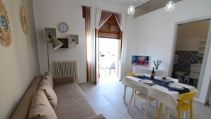 Un salon avec un canapé beige, une table à manger dressée pour quatre personnes et un téléviseur fixé au mur.