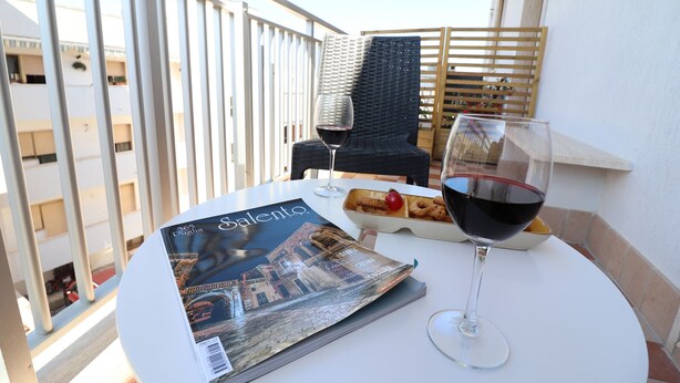 Une table avec un magazine, un verre de vin rouge et une petite assiette de nourriture sur un balcon.