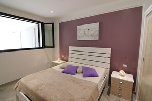 Une chambre à coucher comprenant un lit, une table de chevet, une œuvre d’art accrochée au mur et une fenêtre.