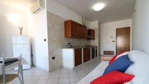 A compact living space with a kitchenette, a dining area, and a sofa with patterned cushions. - Casa Vanessa – Modern one-bedroom apartment with sea view in central Otranto (Otranto)