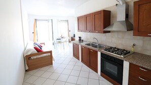 A kitchen with wooden cabinets, a gas stove, a sink, and a tiled floor. - Casa Vanessa – Modern one-bedroom apartment with sea view in central Otranto (Otranto)