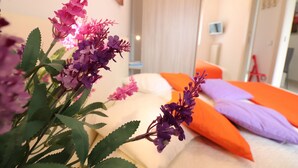 Une chambre d’hôtel avec un lit, des oreillers et une plante aux fleurs violettes.