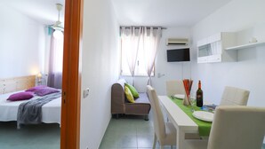 Ein gemütlicher Raum mit Bett, Sofa, Esstisch mit Stühlen und einem an der Wand befestigten Fernseher.