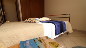 A neatly made bed with a white quilt and blue blanket, a wooden door in the background, and a brochure on the floor. - Casa vacanze "clio" centro Otranto, Salento 6 posti (Otranto)