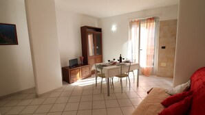 A dining area with a table set for two, a cabinet with a television, and a red sofa. - Casa vacanze "clio" centro Otranto, Salento 6 posti (Otranto)