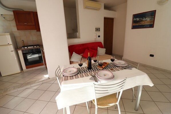 A dining area with a table set for four, a kitchen with a stove and oven, and a red chair.