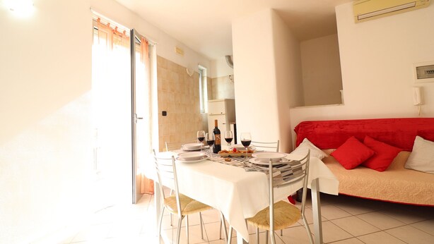 A dining area with a table set for four, a red sofa, and a kitchen in the background. - Casa vacanze "clio" centro Otranto, Salento 6 posti (Otranto)