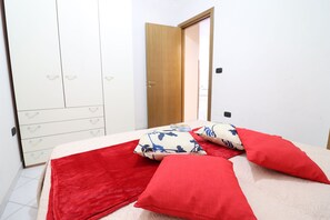 Una camera da letto con un letto, cuscini rossi, un armadio bianco e una porta in legno.