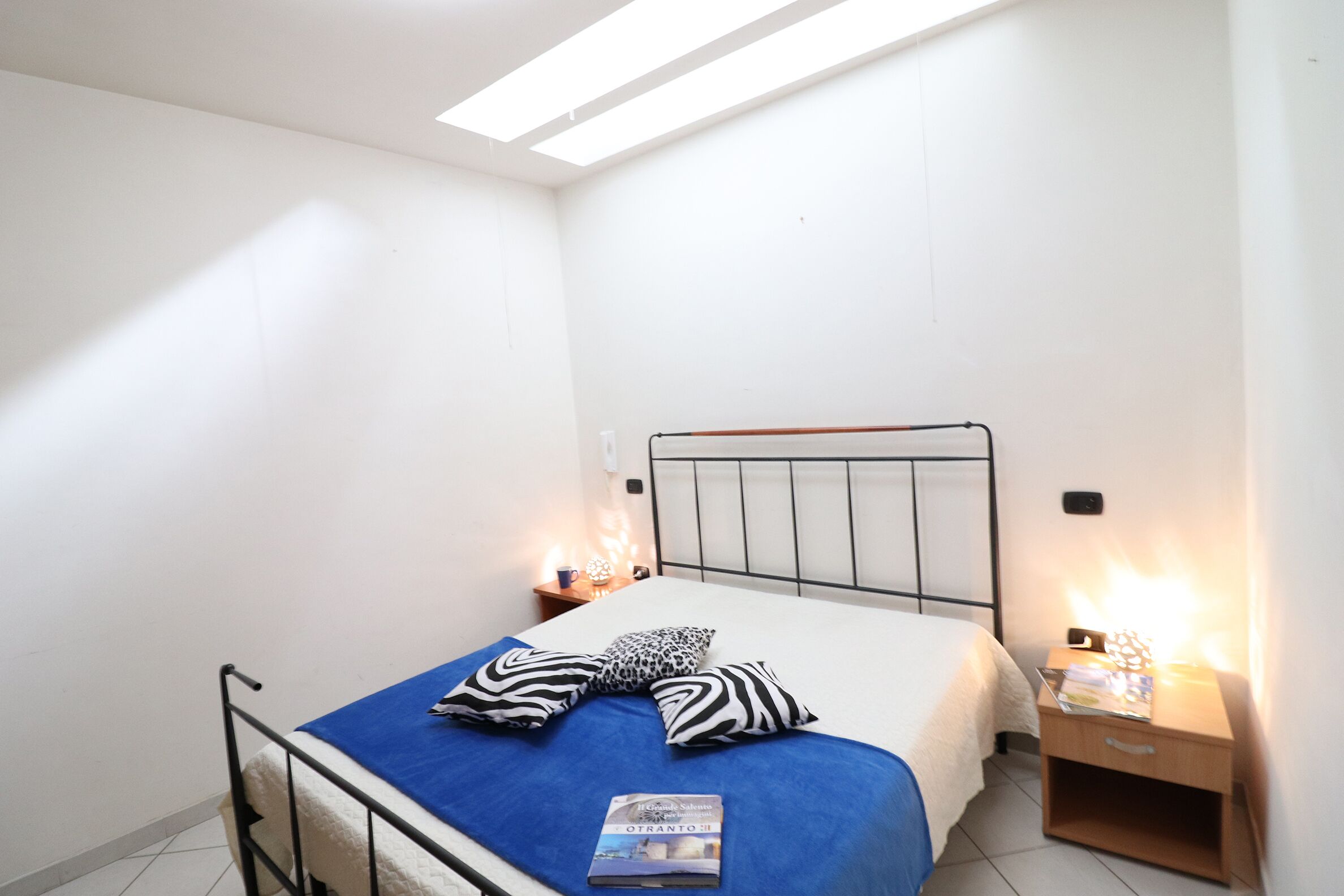 A bedroom with a bed, two pillows, a bedside table with a lamp, and a nightstand with a lamp.