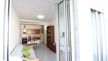 Een knus woongedeelte met een kitchenette, een eethoek en een bed met groene kussens.