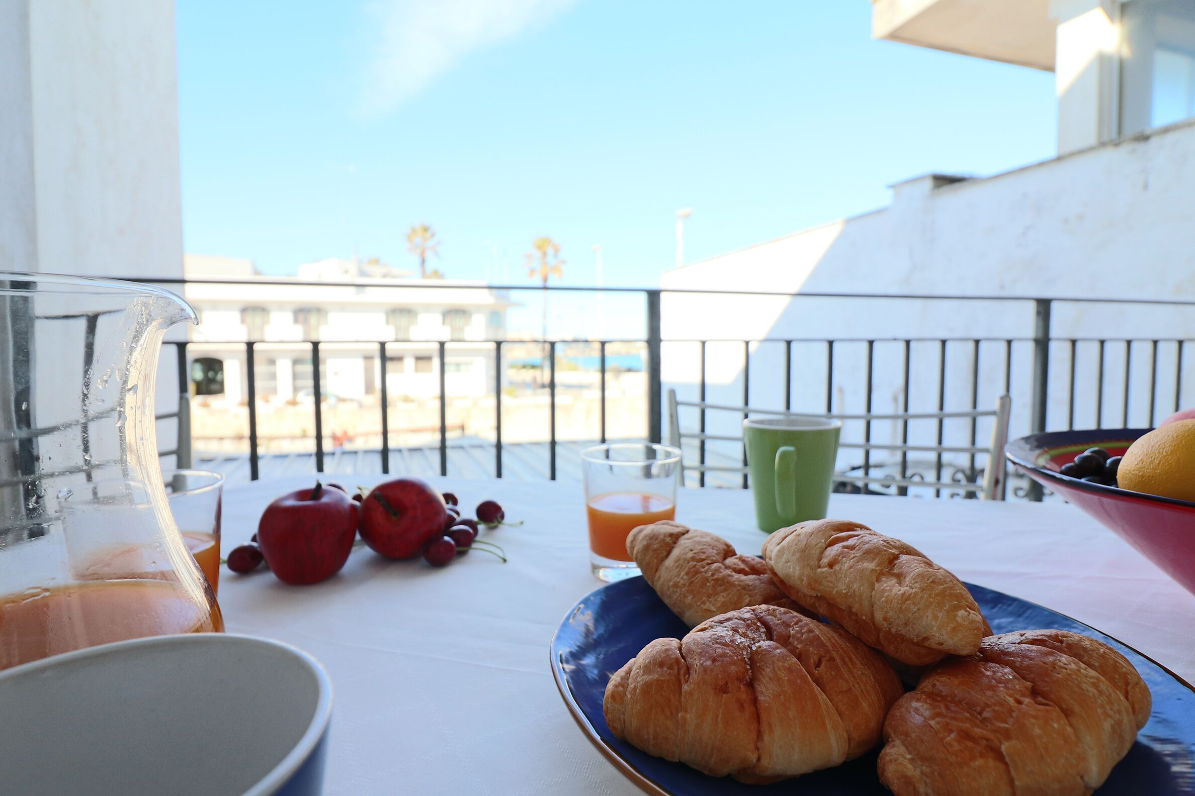 Een balkon met een ontbijttafel, inclusief croissants, een fruitschaal en een glas sinaasappelsap.