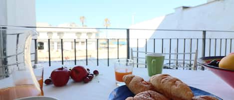 A balcony with a table set for breakfast, including croissants, a bowl of fruit, and a glass of orange juice.