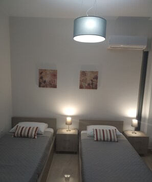 Habitación de hotel con dos camas individuales, mesitas de noche con lámparas, una luz de techo y dos obras de arte colgadas en la pared.