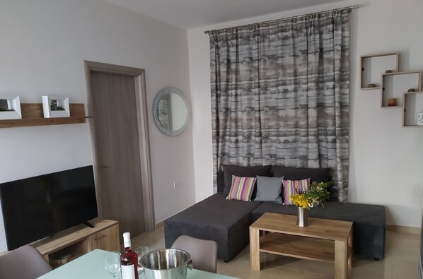 Una sala de estar moderna con un televisor de pantalla plana, una mesa de centro de madera, un sofá y una mesa de comedor.