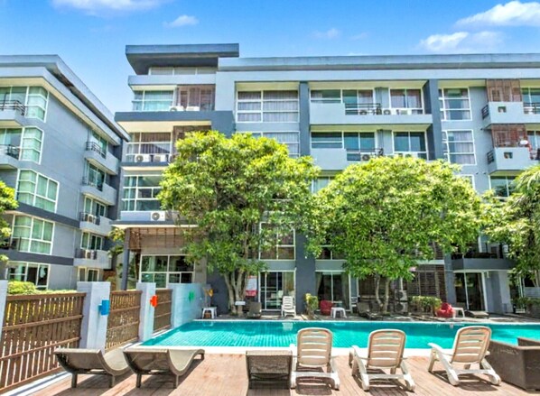 A modern multi-story hotel with a swimming pool, outdoor seating, and lush greenery.