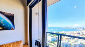A room with a view of a cityscape and the ocean, a brown leather sofa, and a framed picture on the wall. - 3008 - Luxurious Ocean View 1BR Apartment in Muang Pattaya, Thailand (Muang Pattaya)