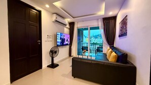 Ein modernes Wohnzimmer mit Sofa, Fernseher, Ventilator und Blick auf einen Balkon mit Sitzmöbeln.