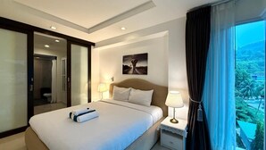 Ein Hotelzimmer mit Bett, Nachttisch, Lampe, einem Gemälde an der Wand und Blick ins Freie.