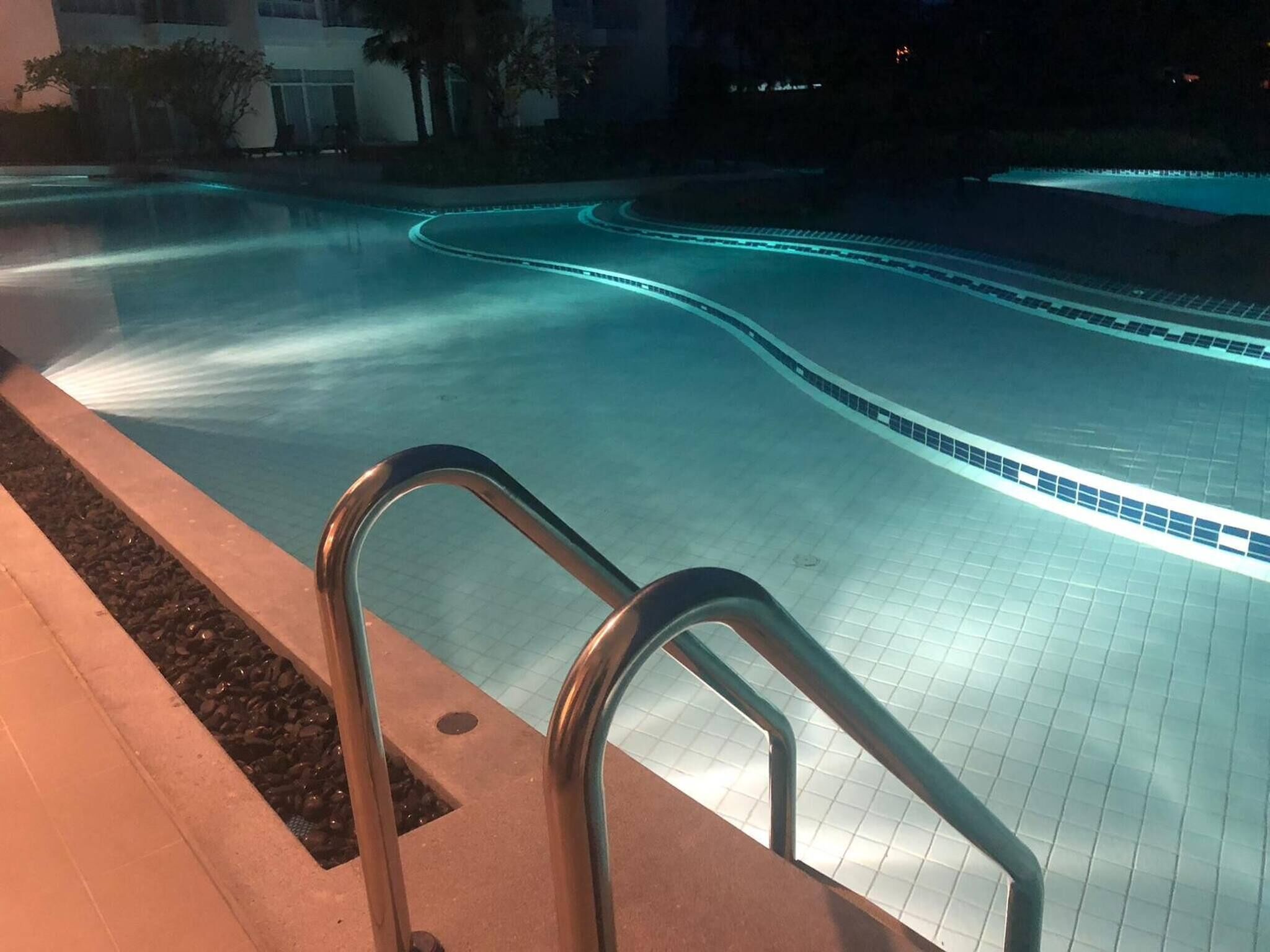 A swimming pool with a curved design, surrounded by a tiled deck and a metal handrail.