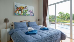 A bedroom with a large bed, a painting of elephants, and a view of a pool and palm trees.