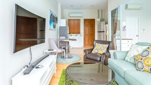 A modern living room with a flat-screen TV, a sofa, a coffee table, and a dining area with a small table and chairs.