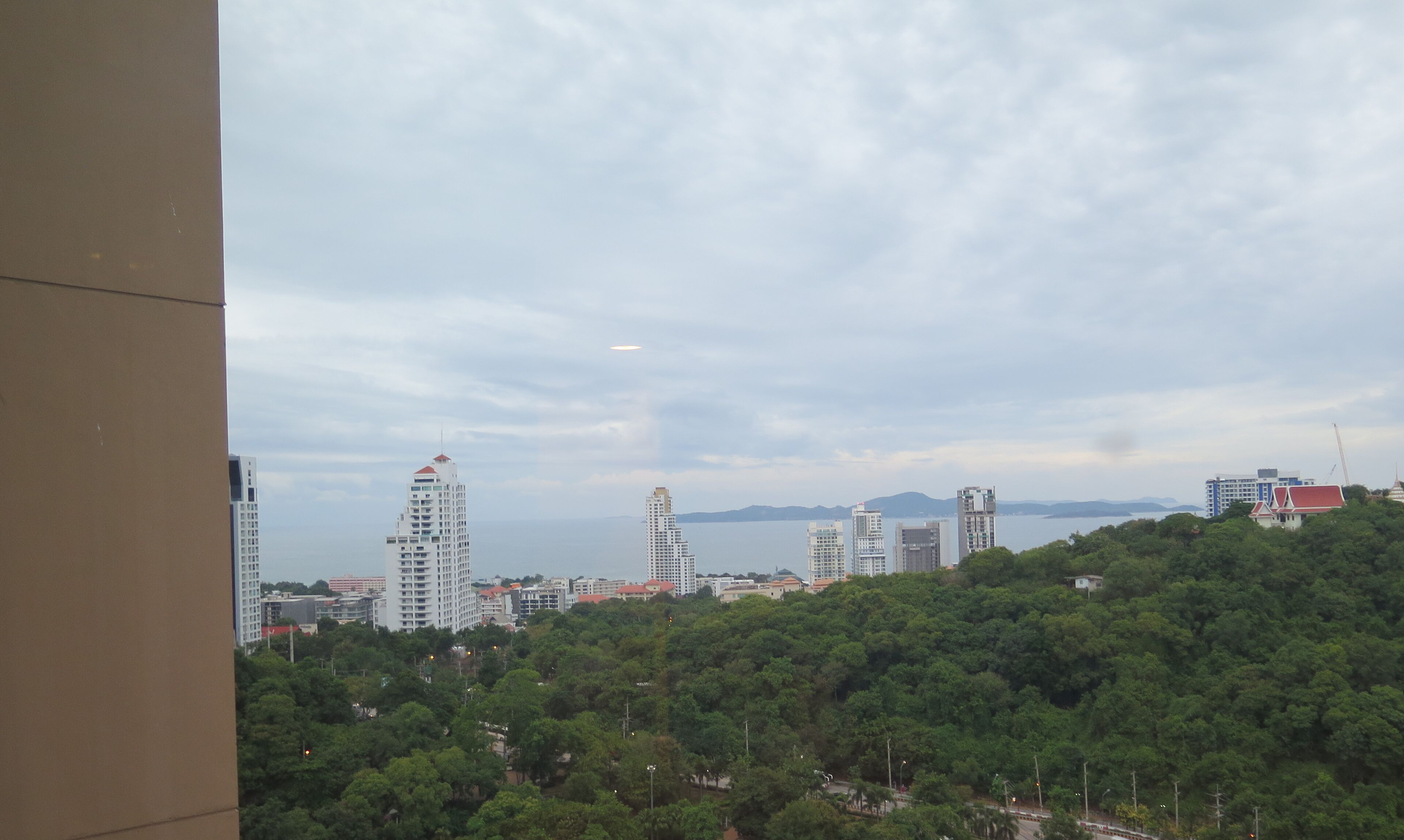A cityscape with tall buildings, a body of water, and a mountainous background.