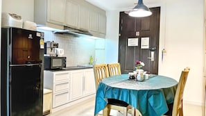 A compact kitchen with a refrigerator, microwave, and stove, a dining table with chairs, and a dark door with a light fixture.