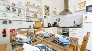 Une cuisine moderne avec des meubles blancs, un four encastré et un coin repas aménagé pour quatre personnes, avec une table dressée pour le repas.