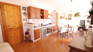 Une cuisine avec des meubles de rangement en bois, une table à manger, des chaises et un réfrigérateur.