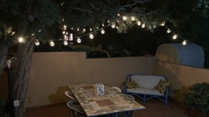 An outdoor patio with a table and chairs, a blue sofa, and string lights. - Casa Gianni Cala Gonone Mare (Sardegna)