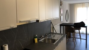 Cozinha moderna com armários brancos, painel de parede de mármore preto, pia de aço inoxidável e um pequeno espaço bar com banquetas.