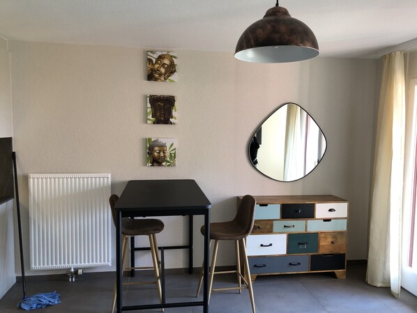 A room with a dining table, two bar stools, a mirror, a radiator, and a cabinet with drawers.