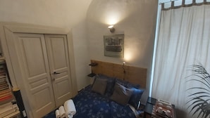 Un dormitorio con cama, mesita de noche, lámpara de pared, una puerta y una ventana con cortinas.