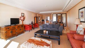 A spacious living room with a large grey sectional sofa, a wooden entertainment unit with a flat-screen TV, and a red armchair.