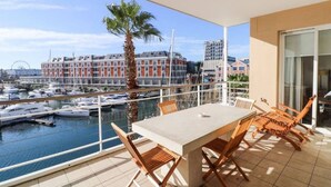 A balcony with a table and chairs overlooking a marina with boats and a Ferris wheel in the background.