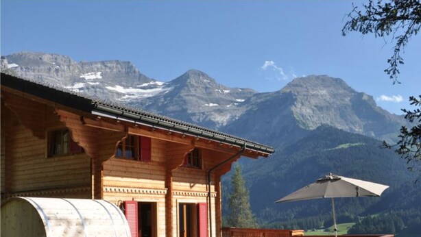 Un chalet en bois avec une grande barrique, une terrasse avec des chaises et une vue sur la montagne.