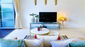 Een moderne woonkamer met een flatscreen televisie, een glazen salontafel en een bank met decoratieve kussens.