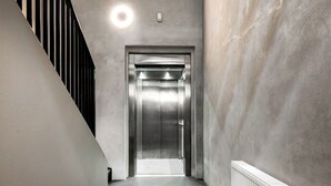 Un ascensor moderno en un pasillo con pared de hormigón y una escalera negra a la izquierda.
