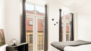 Ein Schlafzimmer mit einem Bett, einer schwarzen Regaleinheit und Blick auf ein rotes Ziegeldach durch eine Schiebetür.
