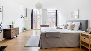 Un dormitorio moderno con una cama grande, un aparador, una mesita de noche y vistas de la ciudad a través de la ventana.