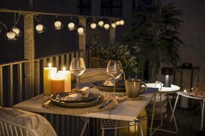 Un espace extérieur aménagé pour les repas, avec des bougies, des verres à vin et une table dressée pour deux personnes.