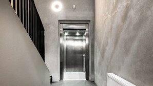 Un ascensor moderno en un pasillo con pared de concreto y escalera de metal.