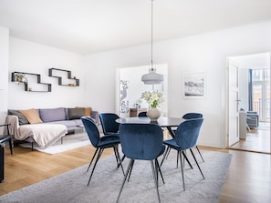Un salon moderne avec un canapé, une table à manger et des chaises, un luminaire suspendu et des œuvres d’art accrochées aux murs.