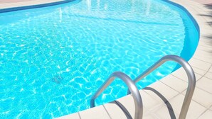 Une piscine d’un bleu éclatant, avec un escalier en métal qui y mène, entourée d’un sol carrelé.