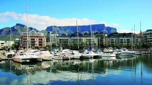 A marina with multiple boats docked, buildings with balconies, and a mountain in the background. - Two Bedroom Apartment - fully furnished and equipped (Cape Town)